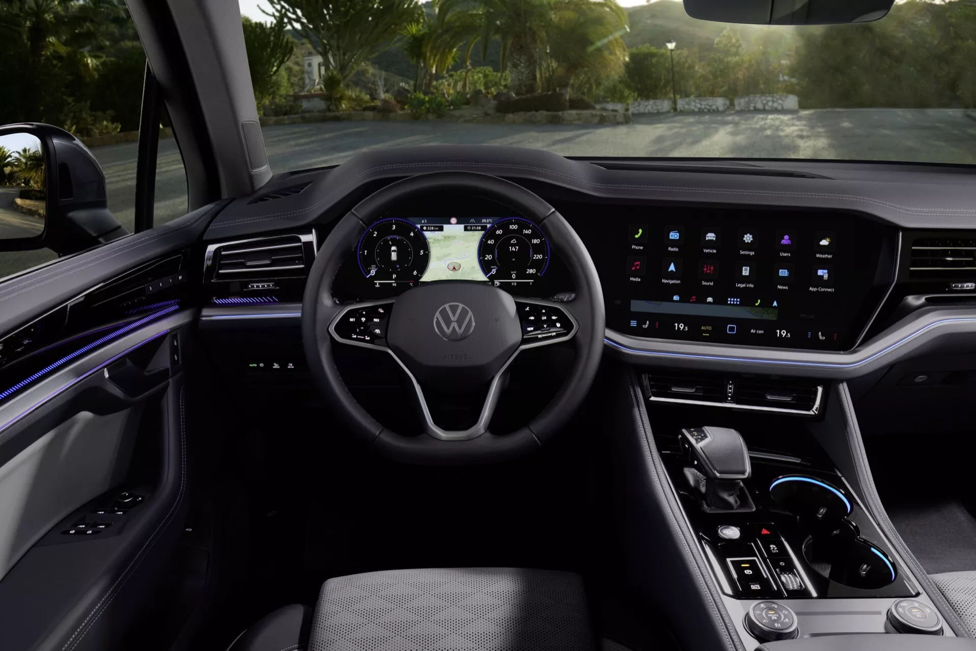 Interiér VW Touareg 2023 z pohľadu vodiča s moderným volantom s tromi ramenami s logom Volkswagen, digitálnym prístrojovým panelom, širokou dotykovou obrazovkou informačného systému, ambientným osvetlením, elegantnou stredovou konzolou s výberom prevodovky a prvotriednymi materiálmi