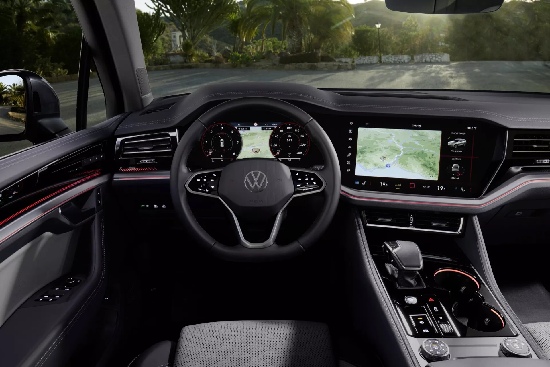 Interiér VW Touareg 2023 so zobrazením volantu s logom Volkswagen, digitálnym prístrojovým panelom, veľkým dotykovým informačno-zábavným systémom na stredovej konzole, ergonomickým sedadlom vodiča vyhotoveným z koženky, a modernými dizajnovými prvkami s červenými akcentami z pohľadu vodiča.