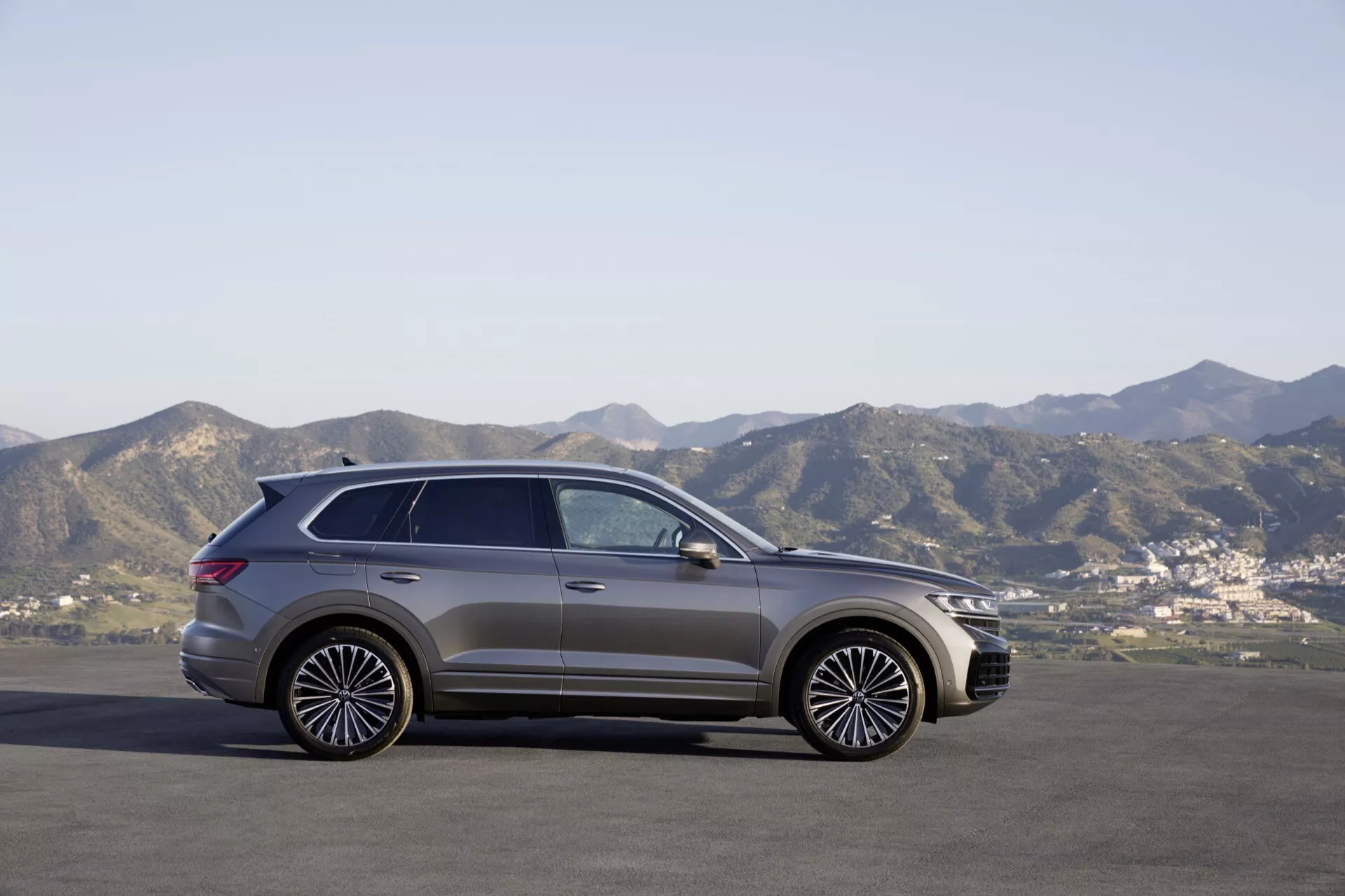 Model VW Touareg III po facelifte z roku 2023 v bočnom profile zaparkovaný na rovnatej ploche oproti horskému pozadiu pod jasnou oblohou, predvádzajúci jeho moderný dizajn SUV, štýlové zliatinové kolesá a panoramatickú strechu.