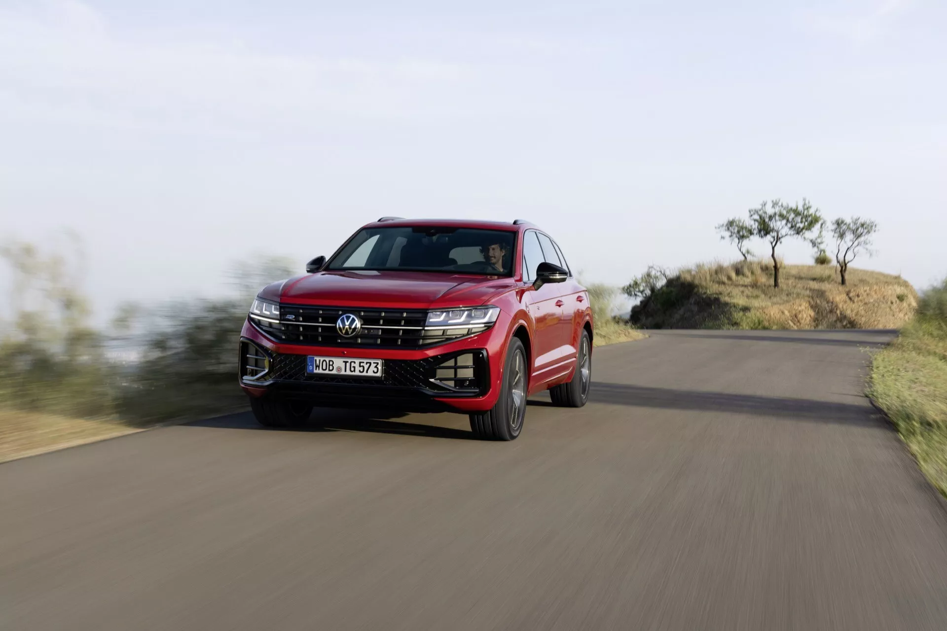 Volkswagen Touareg 2023 v červenej farbe zachytený v pohybe z nízkeho uhla, zdôrazňujúci mriežku chladiča, LED svetlomety a dynamický bočný profil uprostred prírodnej krajiny.
