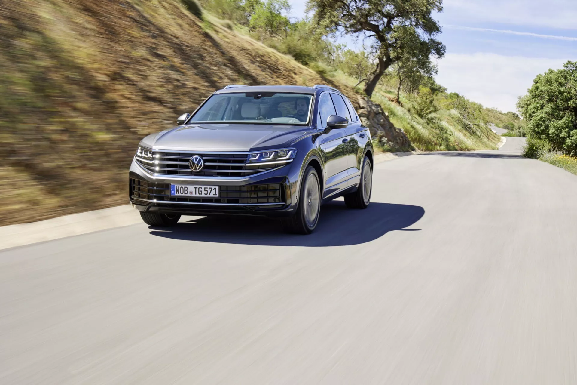 VW Touareg III facelift 2023 zobrazený v dynamickom cestnom prostredí, zdôrazňujúci LED svetlomety, modernú mriežku chladiča, športové zliatinové kolesá a funkcie ADAS.