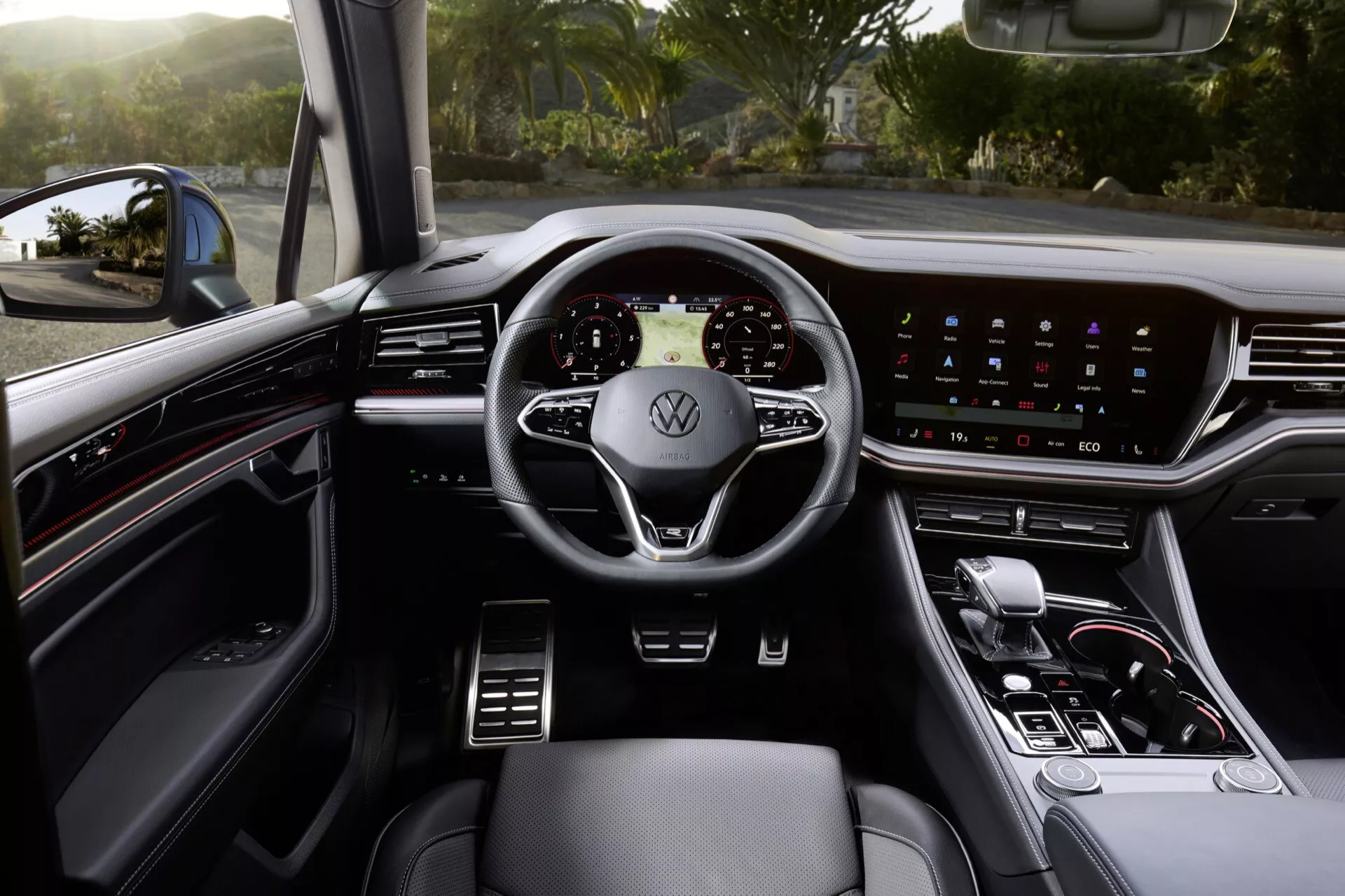 Interiér Volkswagen Touareg 2023 z pohľadu vodičského sedadla ukazujúci moderný trojramenný volant s logom Volkswagen, digitálny prístrojový panel, široký dotykový informačno-zábavný systém na palubnej doske, minimálne fyzické ovládače, páku automatickej prevodovky a prémiové kožené sedadlá s viditeľnými ovládaniami